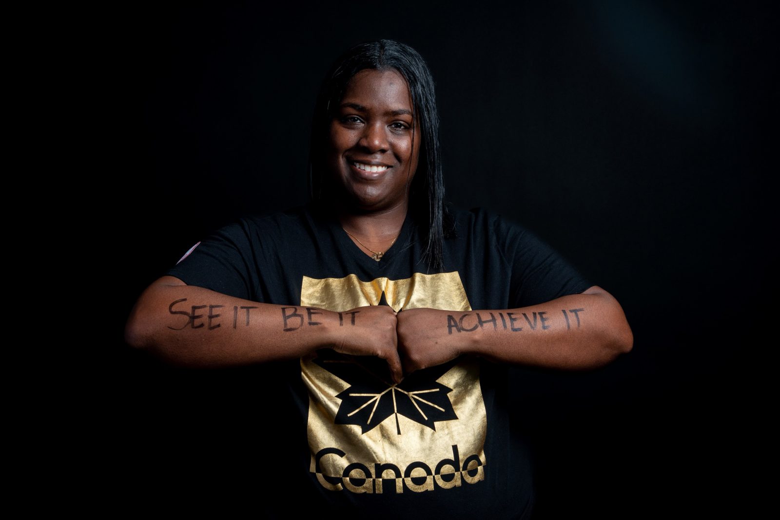 Shauna Bookal holds her arms in front of her chest, knuckles touching each other, to show the message written on her arms, “See it, be it, achieve it.”