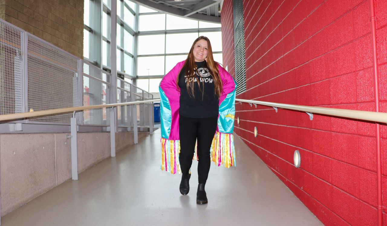 A woman wearing regalia poses for a photo in a sunny hallway.