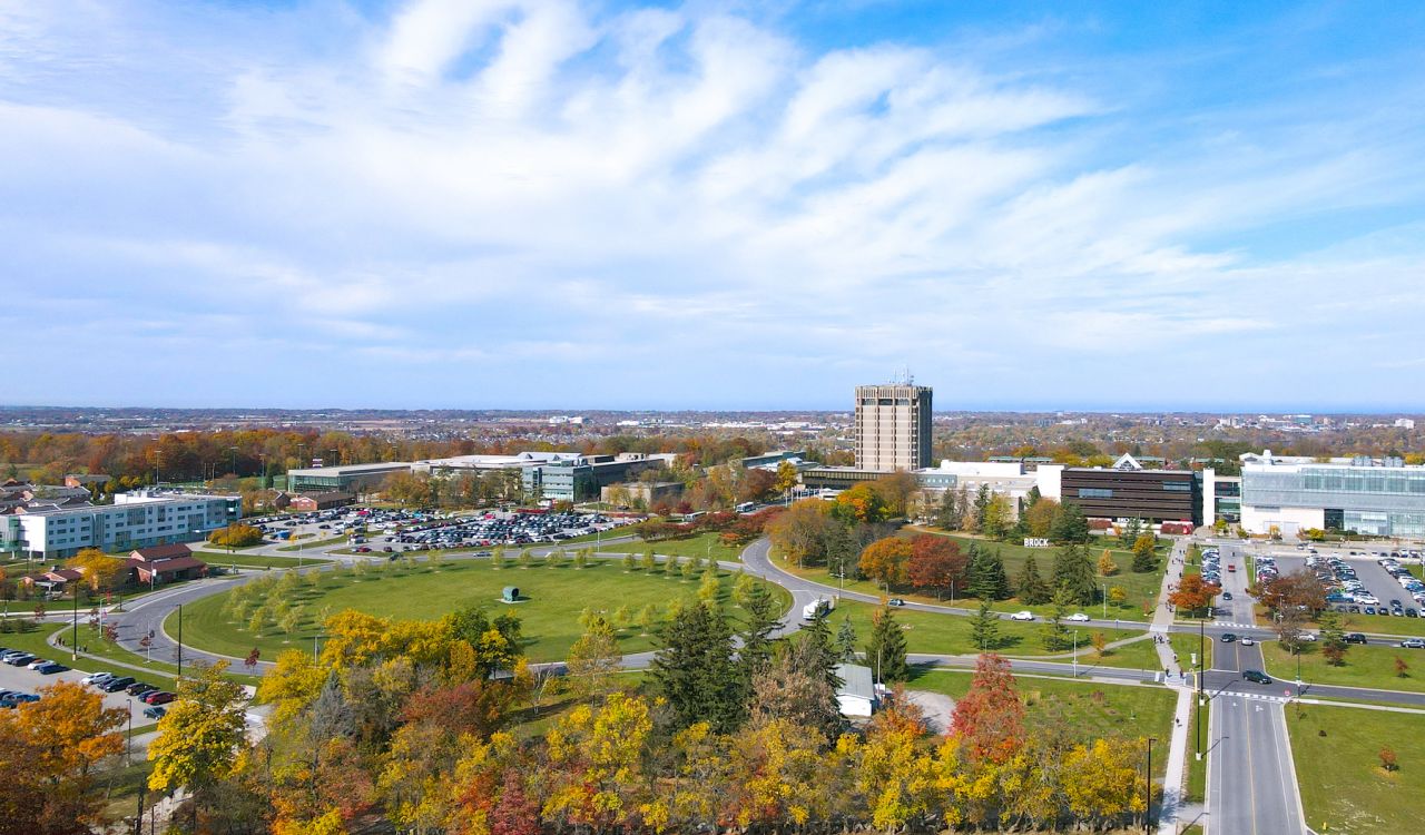 Brock University's main campus seen from an aerial view with an abundance of green space and trees in the foreground. 