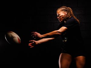 A woman throws a rugby ball under dramatic lighting.