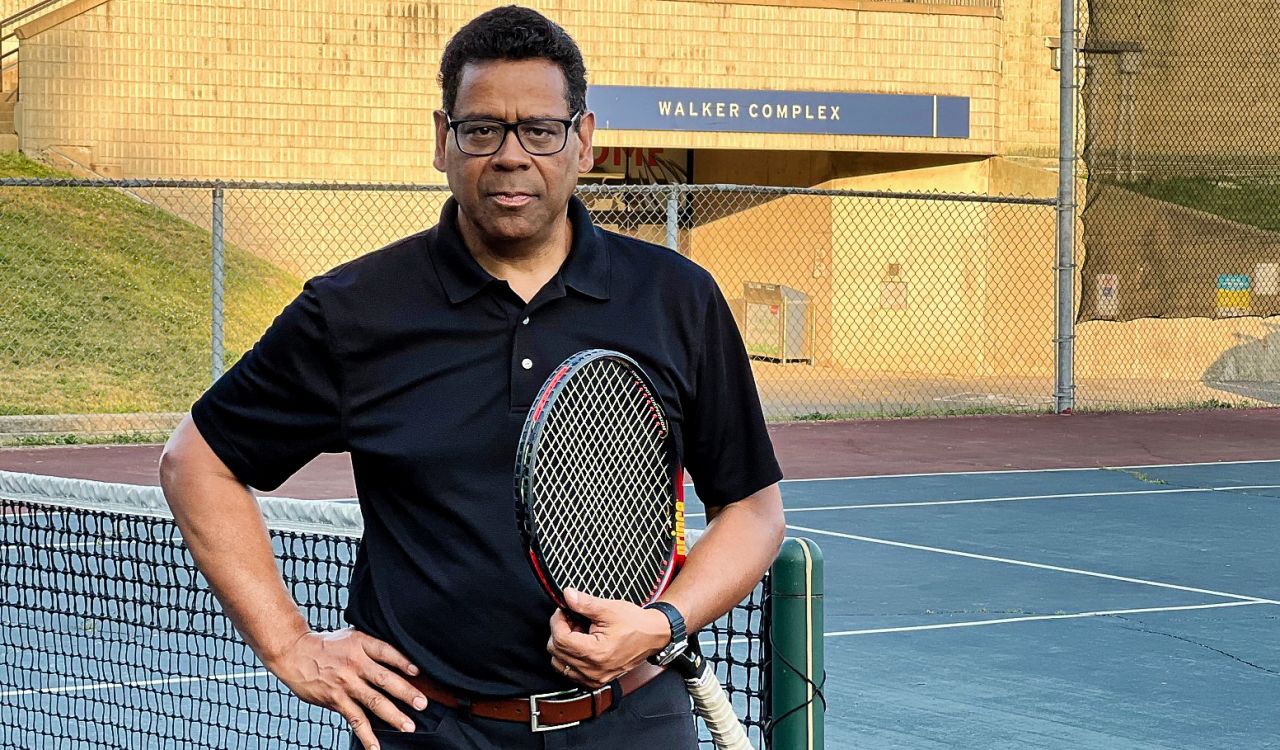 A man stands on a tennis court holding a racquet at Brock University.