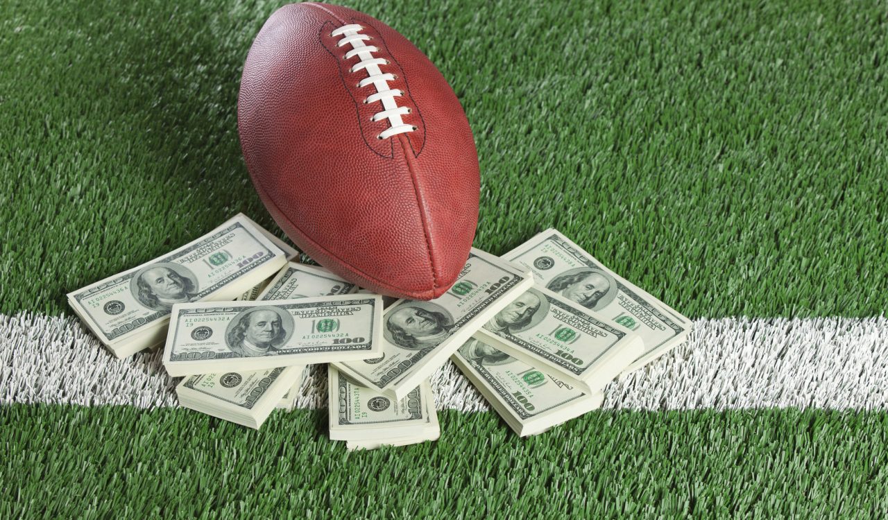 An football sits with a pile of money on a green field