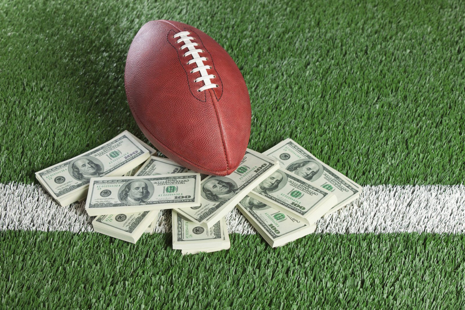 An football sits with a pile of money on a green field