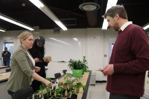 A woman (left) and a man (right) stand on either side of a table full of small plants.