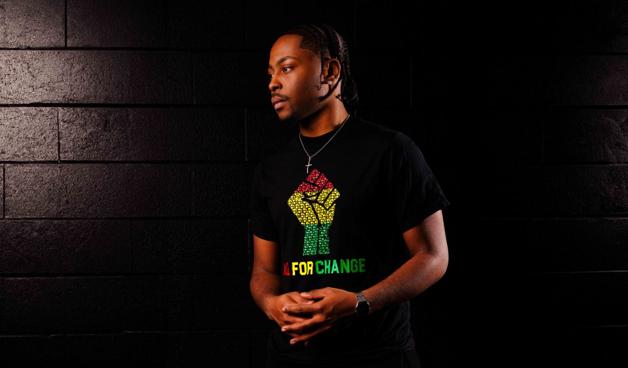 A man stands in the dark wearing an inclusive t-shirt in honour of Black History Month and African Heritage Month.
