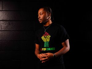 A man stands in the dark wearing an inclusive t-shirt in honour of Black History Month and African Heritage Month.
