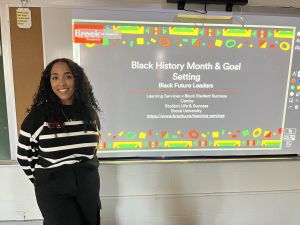 A woman stands ready to give a presentation on Black History Month at the front of a high school classroom.