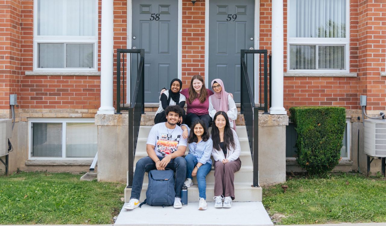 A group of students sit on outdoor steps in front of the entrance to two housing units.