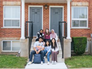 A group of students sit on outdoor steps in front of the entrance to two housing units.