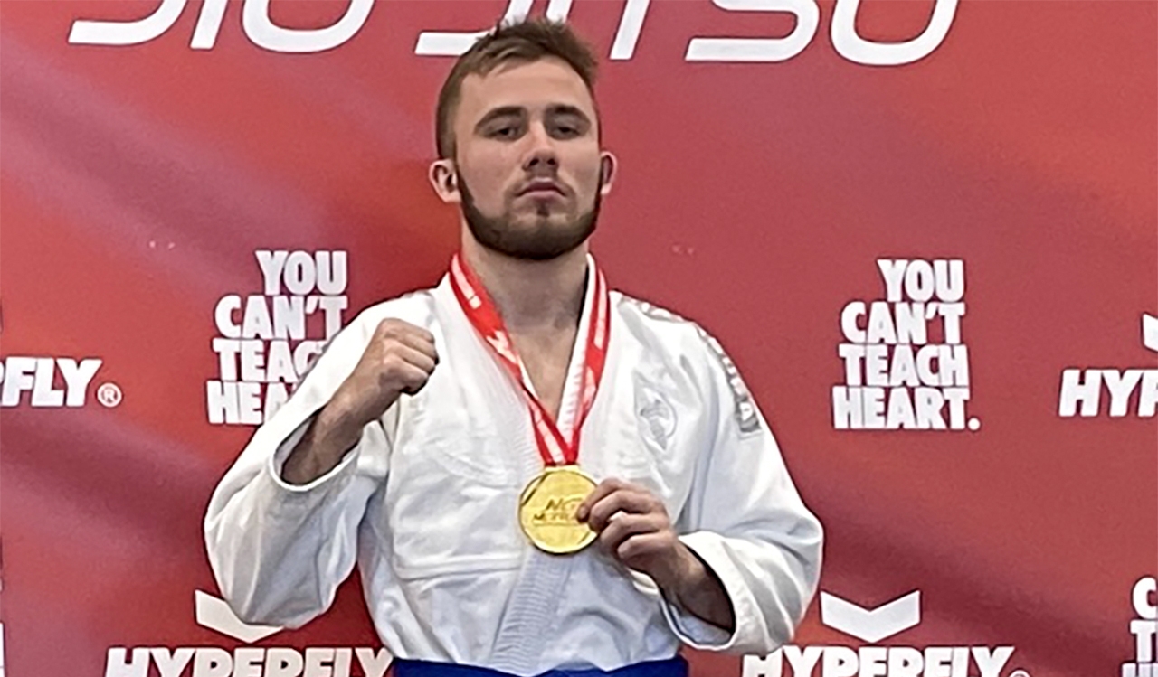 A man in a Jiu Jitsu uniform poses with a gold medal.