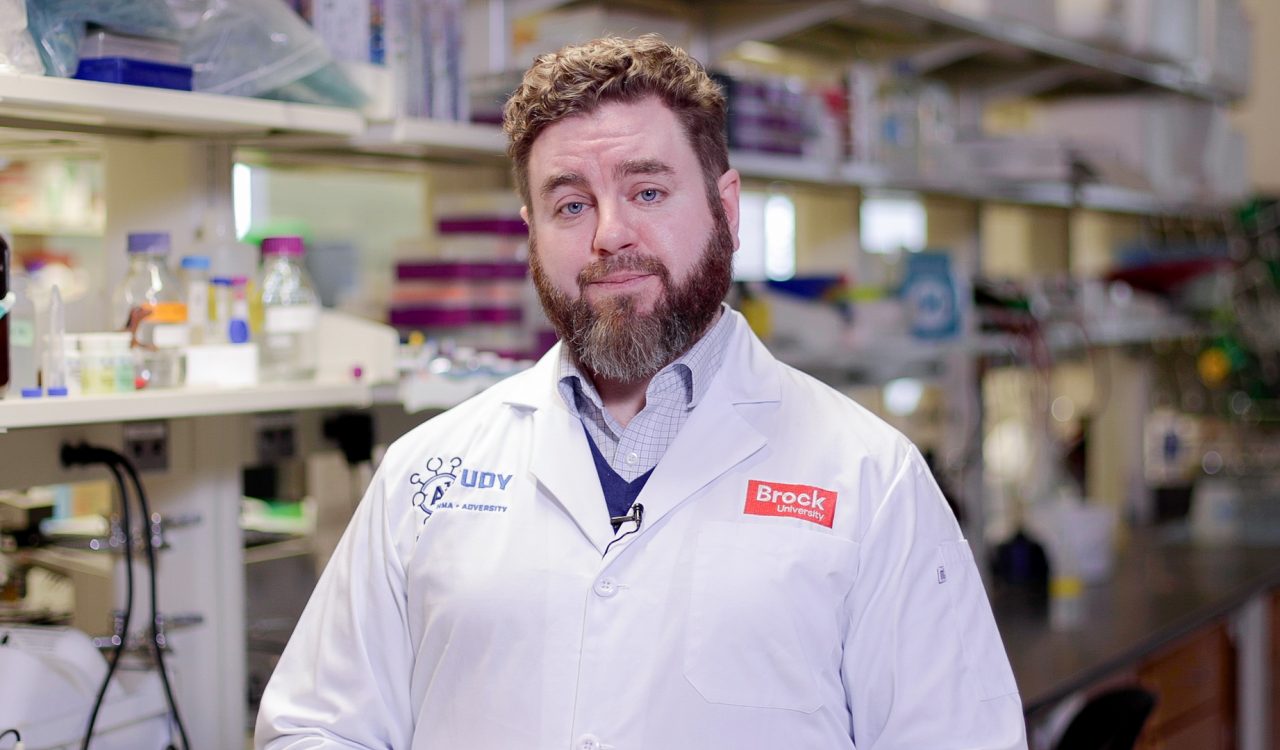 Associate Professor of Immunology Adam MacNeil wears a white laboratory coat in his Inflammation and Immunity Lab at Brock University. 