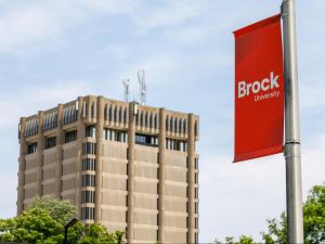 A red Brock University flag hangs from a pole with a concrete tower in the background.