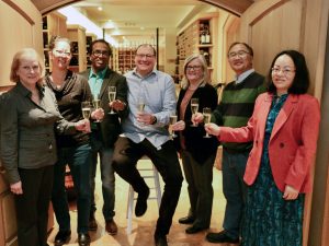 Seven people stand together holding wine glasses.