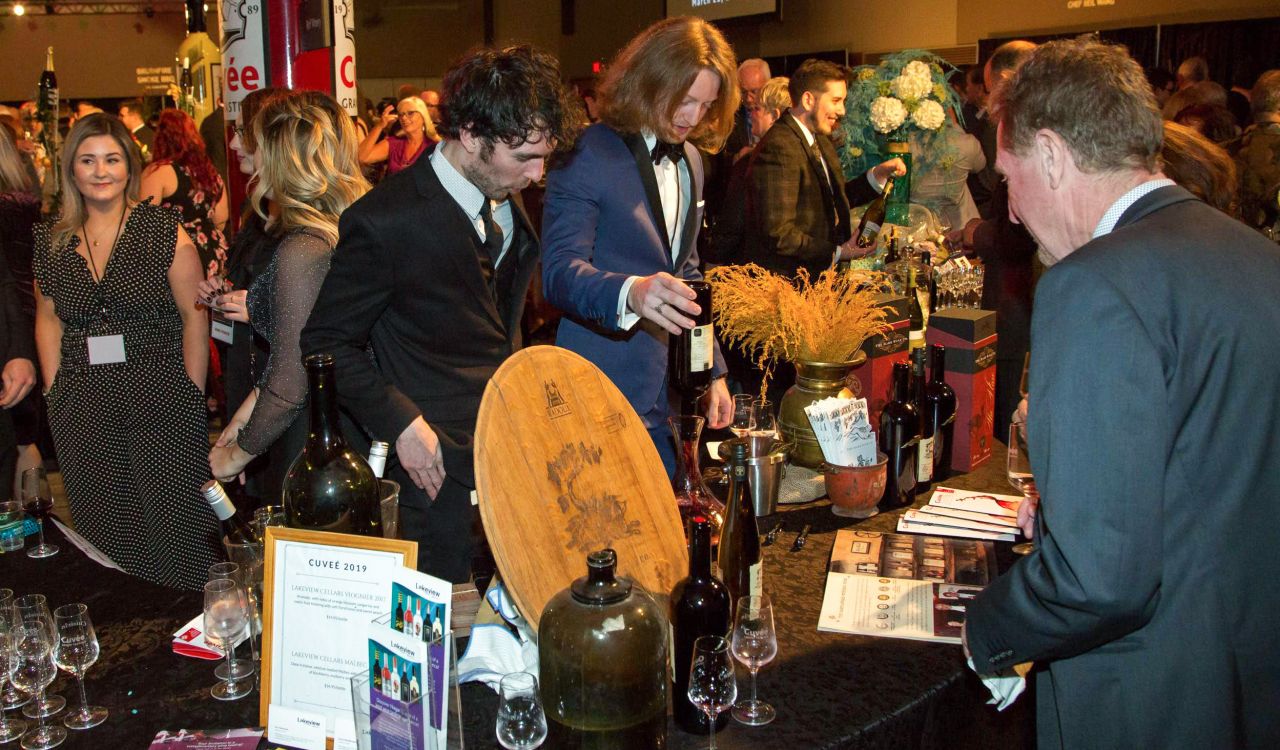 A crowd of people in formal wear sample wine at an event.