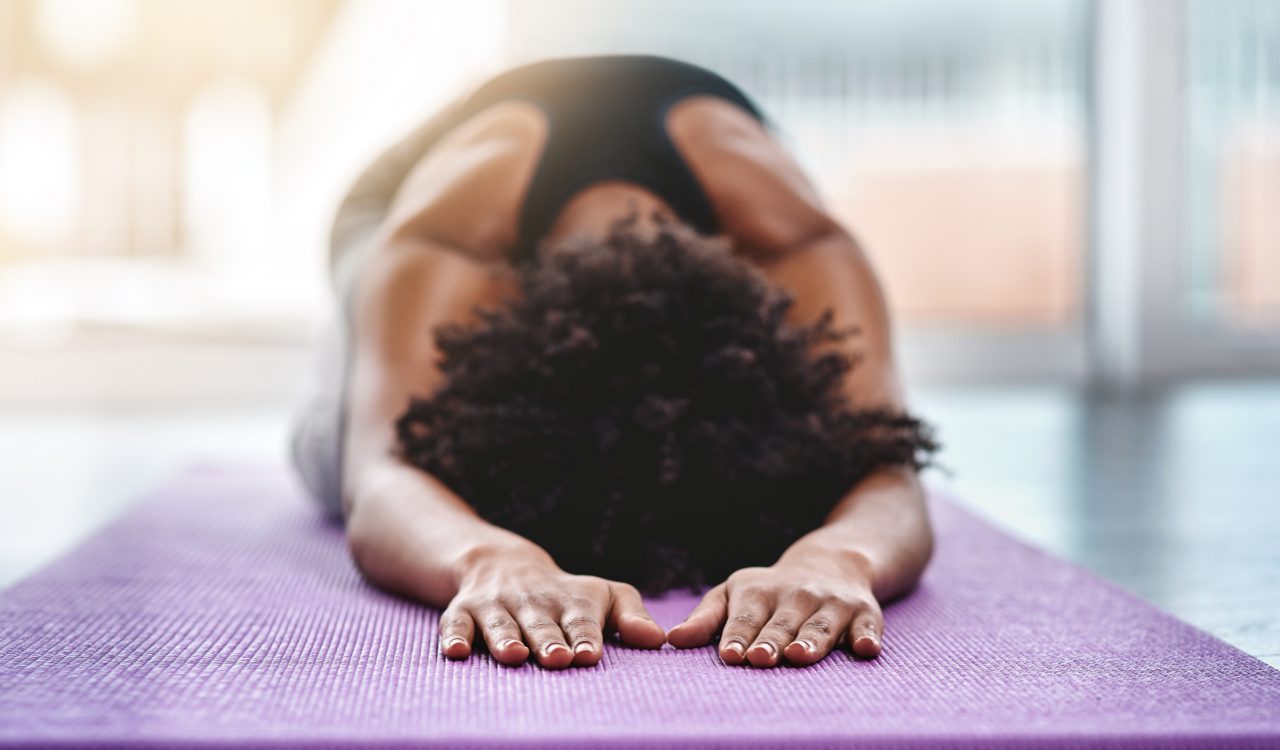 A woman is stretching with her face down on a yoga mat.