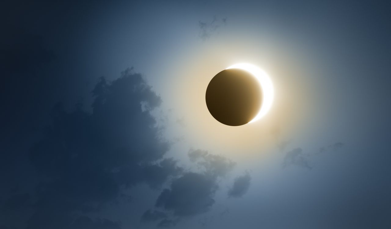 A solar eclipse with a dark blue sky and clouds.