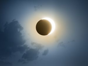 A solar eclipse with a dark blue sky and clouds.
