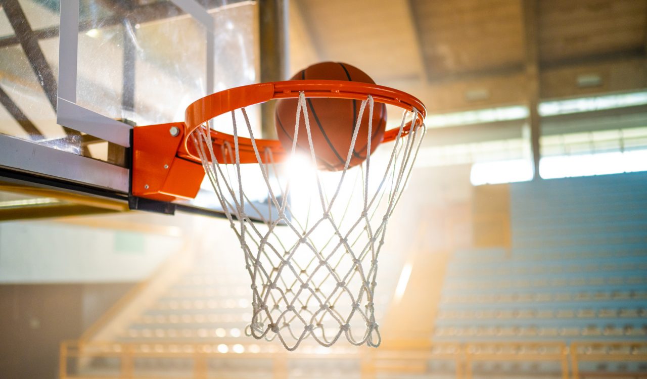 Close-up of basketball in a basketball net with a gym in the background.