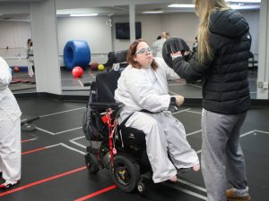A woman stands holding boxing pads as another women in a wheelchair punches them as part of an adaptive marital arts program.
