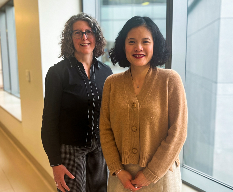 Michelle McGinn and Dr. Jennifer Tsang stand next to each other in a hallway near a window.