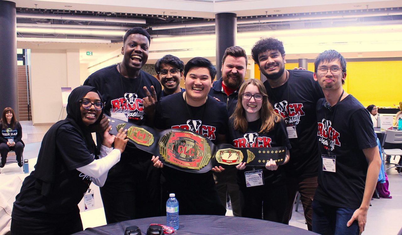 A group of university students hold up a championship belt.