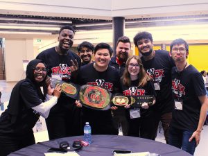 A group of university students hold up a championship belt.