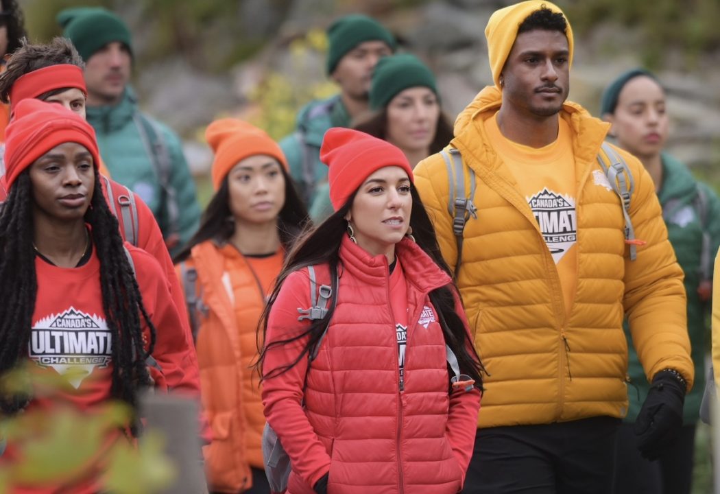 A group of people stand outside, each wearing outdoor gear of different colours including red, orange, green and yellow on CBC’s Canada’s Ultimate Challenge. Standing in the middle of the group, looking serious with her hands in her pockets, is Brock graduate Courtney Copoc-Hopkins.