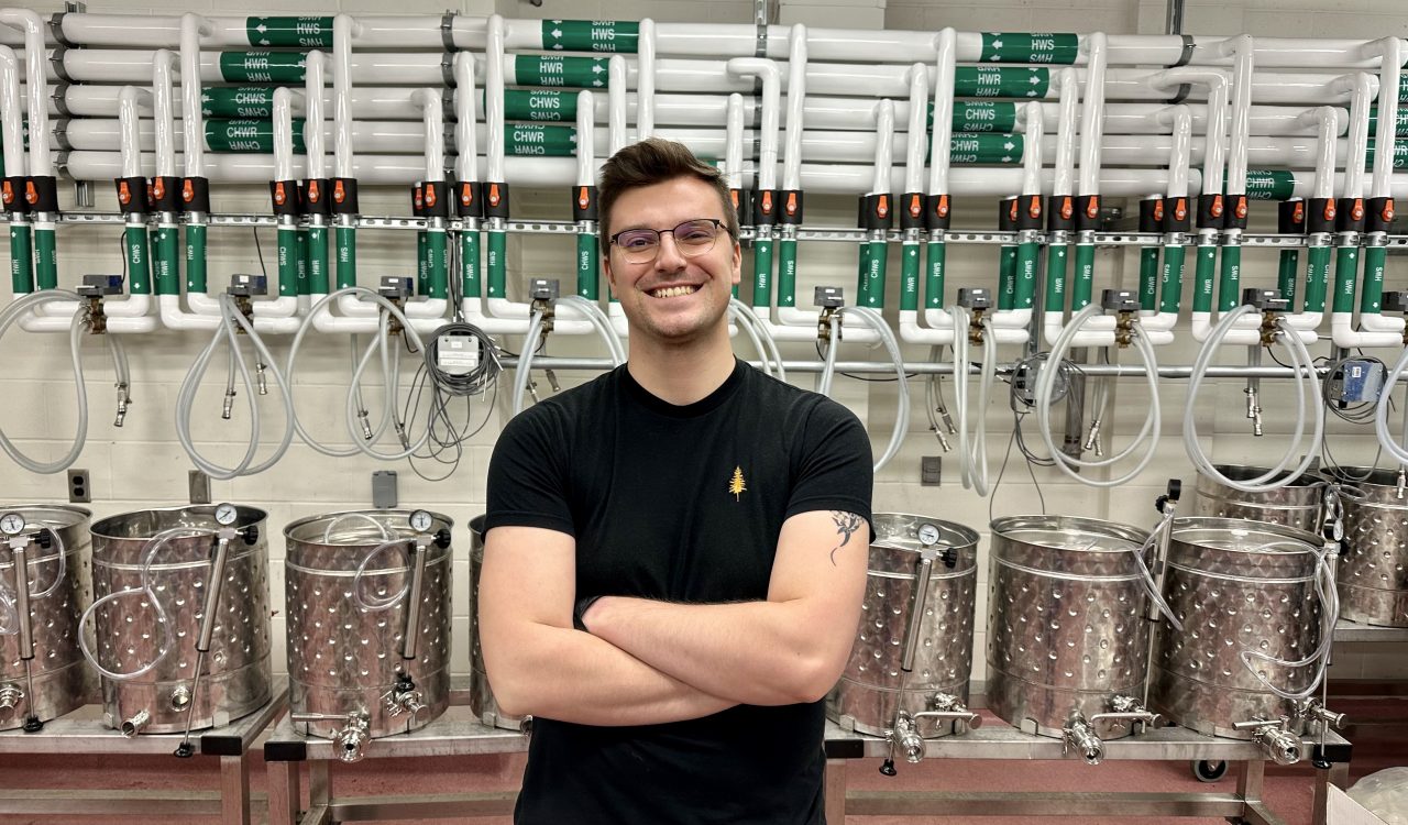 Daniel Phillipow stands in front of a series of steel jacketed fermenter vessels in the winery at Brock University.