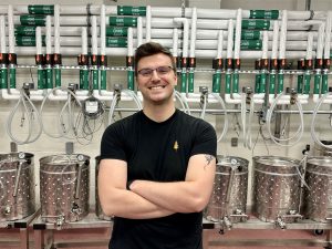 Daniel Phillipow stands in front of a series of steel jacketed fermenter vessels in the winery at Brock University.