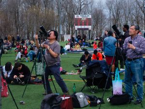 People with cameras on tripods are among those gathered on a football field to watch the total solar eclipse.