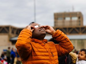 A man wearing eclipse glasses looks up towards the sky.