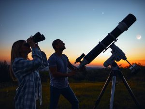 A couple stargazes with a telescope at sunset.