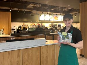 A Starbucks barista holds a bag of coffee grounds in front of a counter.