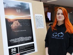 A woman stands in front of a movie poster for the film My Name is Wolastoq.