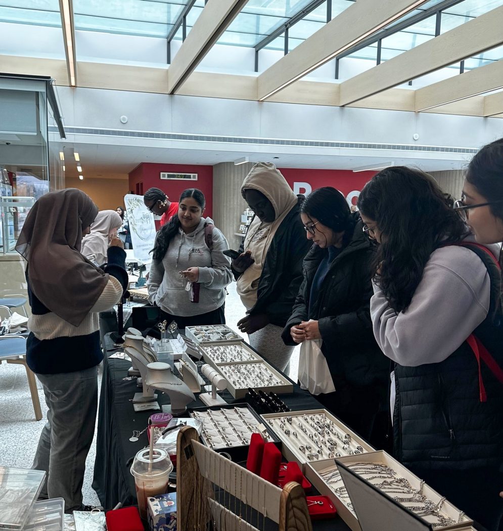 Five students look at jewelry on a table in a vendor market.