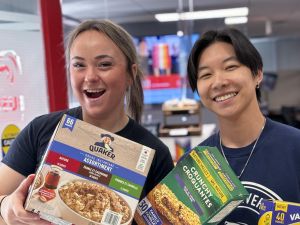 Two university students hold up boxes of oatmeal and granola bars.