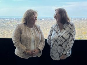 Ontario’s Minister of Agriculture, Food and Rural Affairs Lisa Thompson and Brock President and Vice-Chancellor Lesley Rigg smiling on a balcony on a sunny day, the Niagara region at a distance in the background.