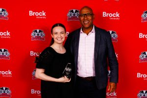 A woman stands holding an award next to a university dignitary at Brock University.