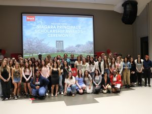 More than 60 high students pose for group photo at the front of an auditorium.