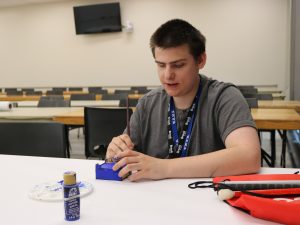 A visually impaired student paints a laser-cut box blue.