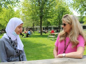 A blind female student sits with a teacher at a picnic table on a university campus.