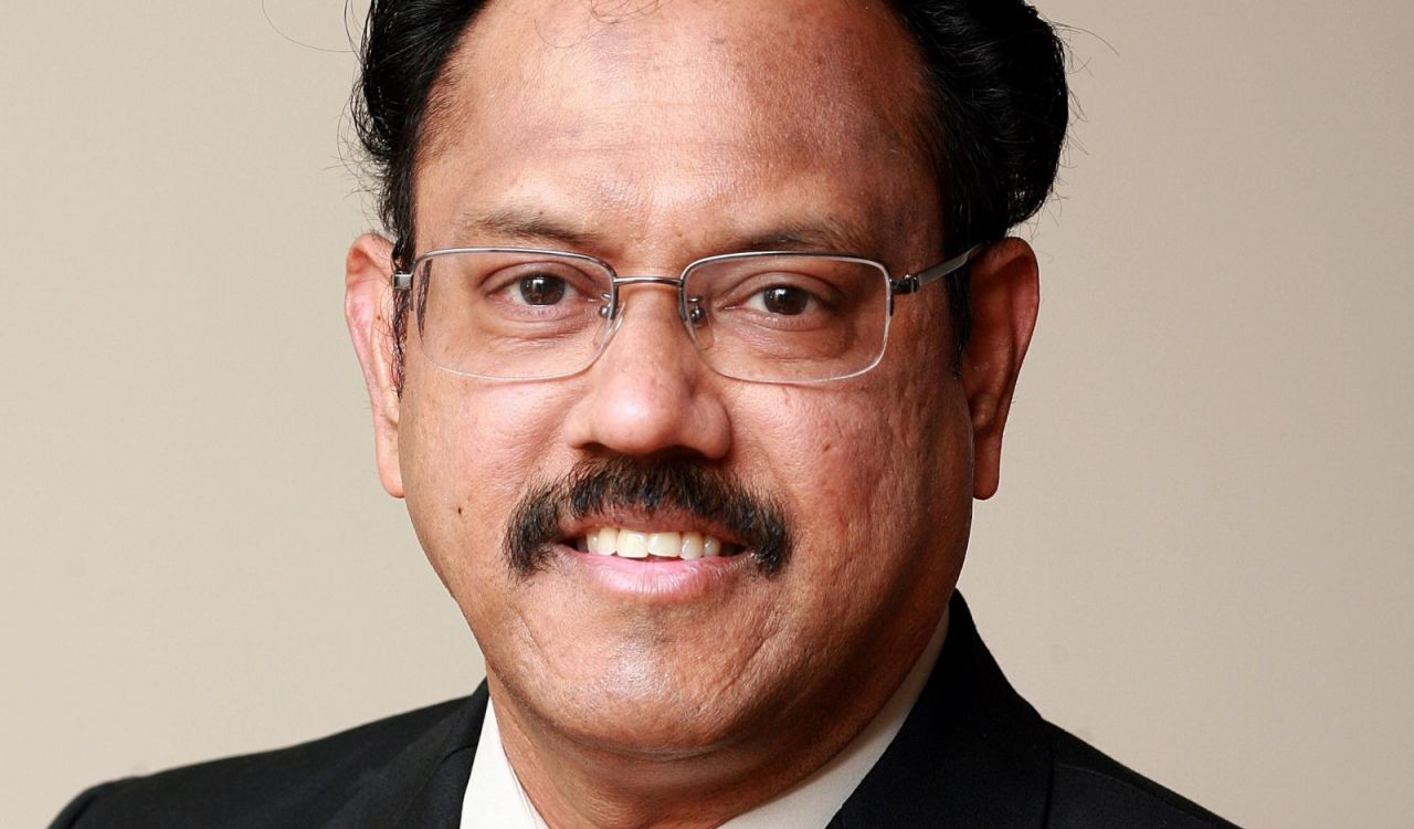 Head and shoulders portrait of V. Kumar smiling into the camera wearing glasses and suit.