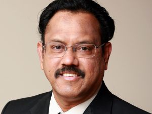 Head and shoulders portrait of V. Kumar smiling into the camera wearing glasses and suit.