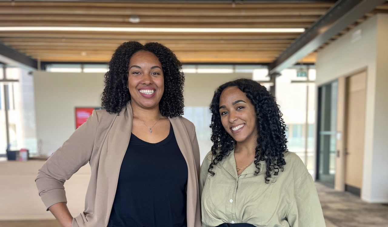 Two women stand beside each other posing for a photo in an office setting.