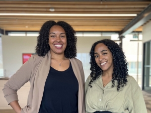 Two women stand beside each other posing for a photo in an office setting.