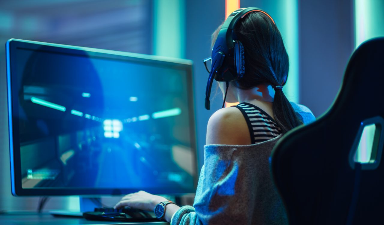 A woman is seen from behind playing a video game, which can be seen on the monitor in front of her.