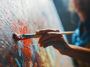 A close-up of a hand holding a paintbrush against a colourful canvas.