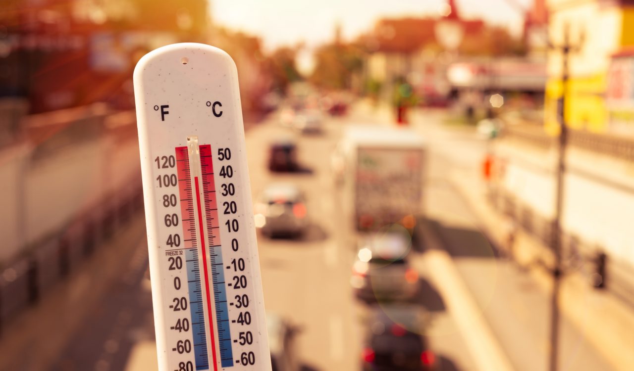 White plastic thermometer held in front of cars and traffic on a busy street during a heatwave