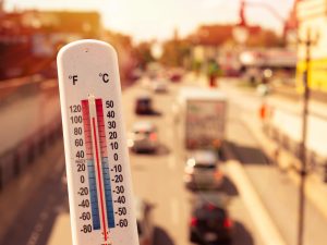 White plastic thermometer held in front of cars and traffic on a busy street during a heatwave