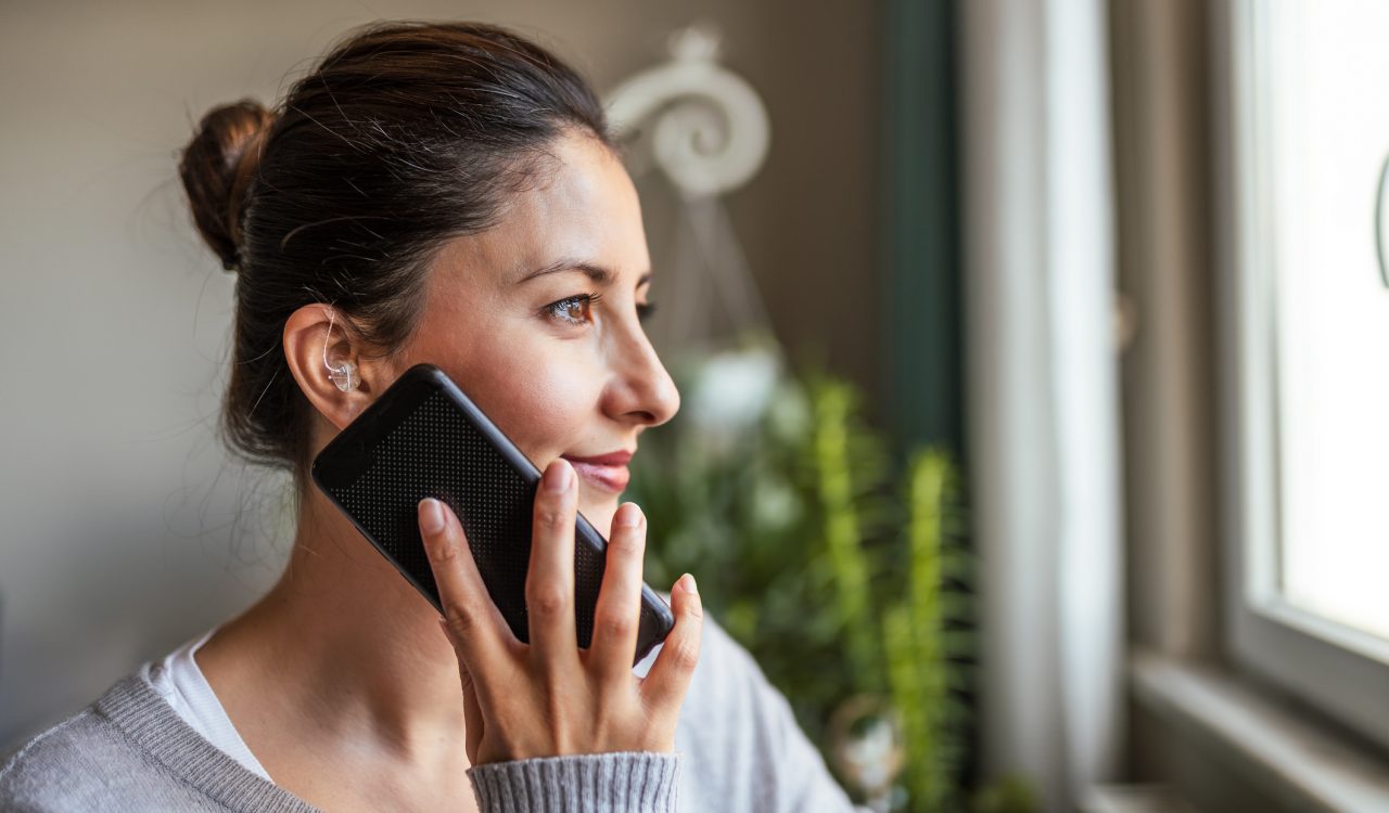 A woman with a hearing aid uses a smartphone.